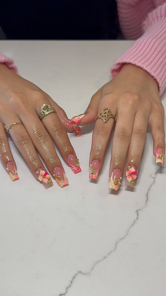 Long pink coffin nails with hibiscus flower charms and gold glitter